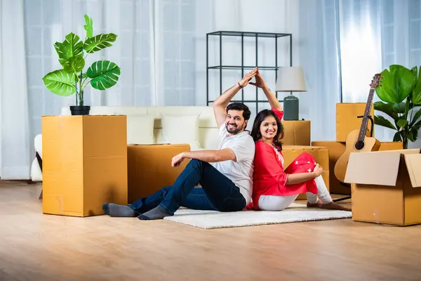 Home moving concept, Indian young couple sitting on floor of living room with cardboard boxes