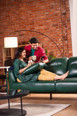 Hintli genç çift evde akıllı telefon kullanıyor.