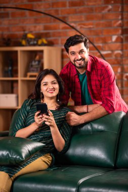 Hintli genç çift evde akıllı telefon kullanıyor.