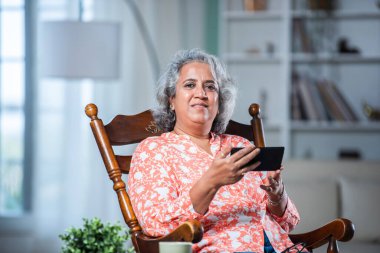 Bir. 40 'lı yaşlarda, beyaz saçlı, akıllı telefon kullanan, sallanan sandalyede oturan Asyalı bir kadın.