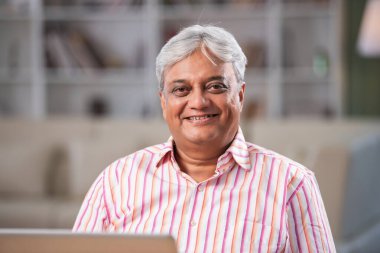 Mutlu Hintli son sınıf öğrencisi evde dizüstü bilgisayar kullanırken kameraya bakıyor.