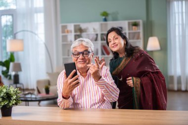 Hintli emekli çift evde akıllı telefon kullanıyor.