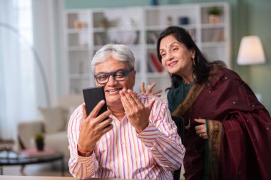 Hintli emekli çift evde akıllı telefon kullanıyor.