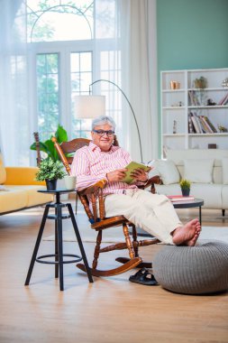 Hintli Asyalı ihtiyar evde sallanan sandalyede otururken kitap ya da roman okuyor.