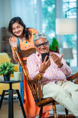 Hintli emekli çift evde akıllı telefon kullanıyor.