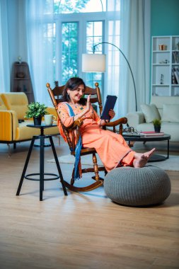 Evde dijital tablet ya da dizüstü bilgisayar kullanan yaşlı Hintli kadın. Teknoloji kavramı ve yaşlılar.