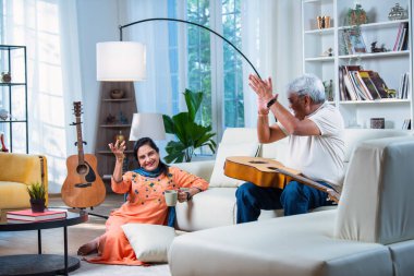 Yaşlı Hintli çift evde gitar çalarken birlikte şarkı söylüyor ve boş zamanların tadını çıkarıyor.