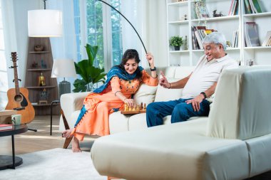 Hintli üst düzey bir çift evde kanepede satranç oynuyor.