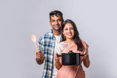Ahşap ve metal mutfak aletleri olan gülümseyen Asyalı genç çiftin portresi.