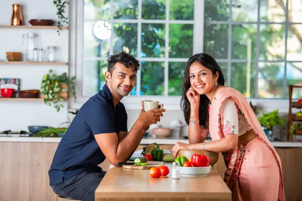 Indian asian young couple having tea or coffee in the kitchen