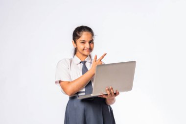 Küçük Hintli Asyalı kız dizüstü bilgisayarda çalışırken beyaz arka planda tek başına duruyor.