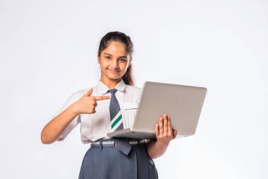 Küçük Hintli Asyalı kız dizüstü bilgisayarda çalışırken beyaz arka planda tek başına duruyor.