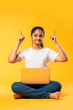 Hintli küçük kız dizüstü bilgisayar kullanıyor sarı arka planda tek başına oturuyor.