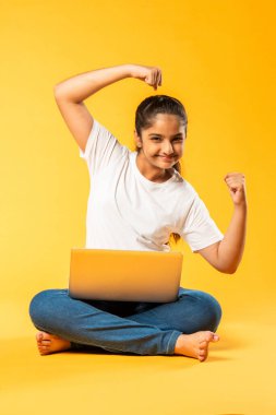 Hintli küçük kız dizüstü bilgisayar kullanıyor sarı arka planda tek başına oturuyor.