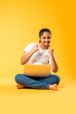Hintli küçük kız dizüstü bilgisayar kullanıyor sarı arka planda tek başına oturuyor.