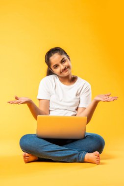 Hintli küçük kız dizüstü bilgisayar kullanıyor sarı arka planda tek başına oturuyor.