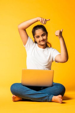 Hintli küçük kız dizüstü bilgisayar kullanıyor sarı arka planda tek başına oturuyor.