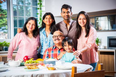 Üç kuşaktır birlikte yemek yiyen Hintli ailenin portresi. Kameraya bakarak.