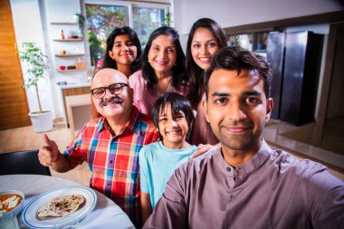 Hintli altı kişilik Asyalı aile öğle yemeği yiyor ve evde selfie çekiyorlar.