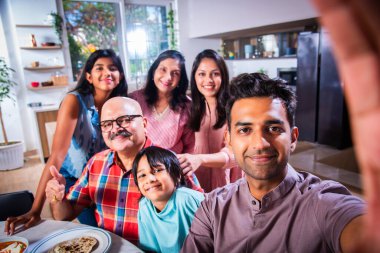 Hintli altı kişilik Asyalı aile öğle yemeği yiyor ve evde selfie çekiyorlar.