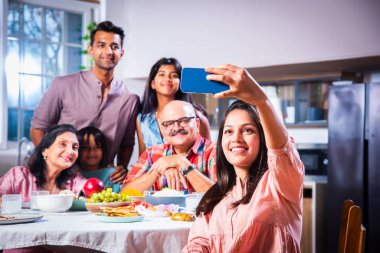 Hintli altı kişilik Asyalı aile öğle yemeği yiyor ve evde selfie çekiyorlar.