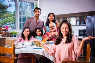 Üç kuşaktır birlikte yemek yiyen Hintli ailenin portresi. Kameraya bakarak.