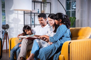 Dört kişilik Hintli genç bir aile fotoğraf albümünde fotoğraflara bakıyor ya da kanepede birlikte kitap okuyor.