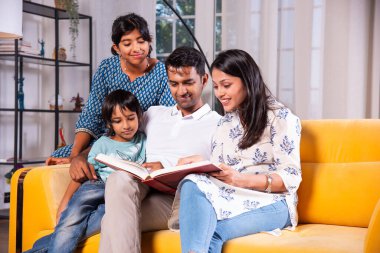 Dört kişilik Hintli genç bir aile fotoğraf albümünde fotoğraflara bakıyor ya da kanepede birlikte kitap okuyor.