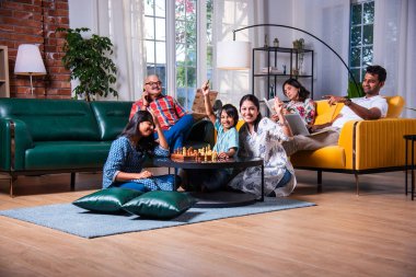 Neşeli Hintli Asyalı çocuklar oturma odasında büyük anne ve babalarıyla satranç oynuyor.