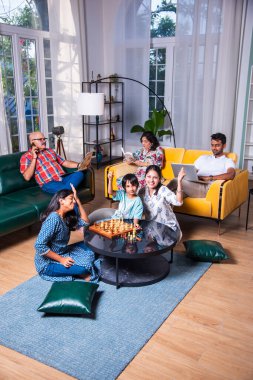 Neşeli Hintli Asyalı çocuklar oturma odasında büyük anne ve babalarıyla satranç oynuyor.