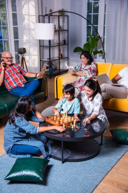 Neşeli Hintli Asyalı çocuklar oturma odasında büyük anne ve babalarıyla satranç oynuyor.