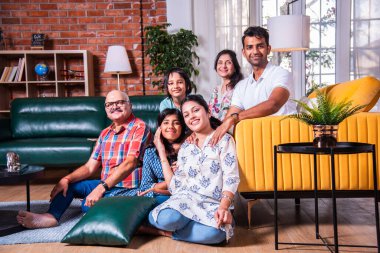 Oturma odasındaki kanepede oturan çok nesilli Hintli ailenin grup fotoğrafı.