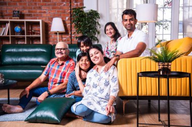 Oturma odasındaki kanepede oturan çok nesilli Hintli ailenin grup fotoğrafı.