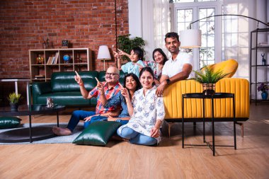 Oturma odasındaki kanepede oturan çok nesilli Hintli ailenin grup fotoğrafı.