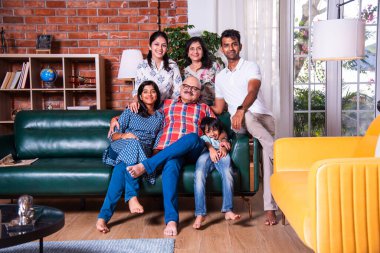 Oturma odasındaki kanepede oturan çok nesilli Hintli ailenin grup fotoğrafı.