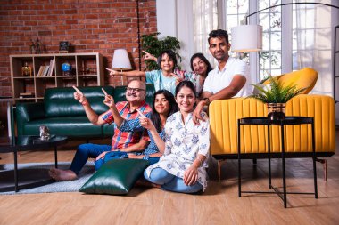 Oturma odasındaki kanepede oturan çok nesilli Hintli ailenin grup fotoğrafı.