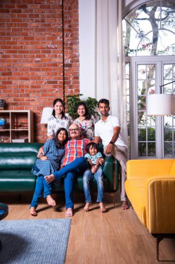 Oturma odasındaki kanepede oturan çok nesilli Hintli ailenin grup fotoğrafı.