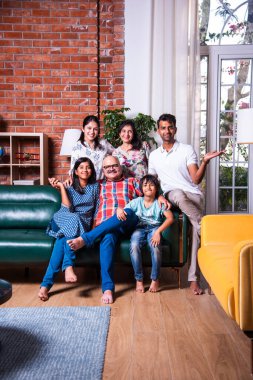 Oturma odasındaki kanepede oturan çok nesilli Hintli ailenin grup fotoğrafı.