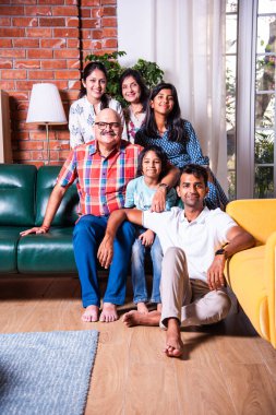 Oturma odasındaki kanepede oturan çok nesilli Hintli ailenin grup fotoğrafı.