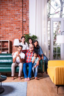 Oturma odasındaki kanepede oturan çok nesilli Hintli ailenin grup fotoğrafı.