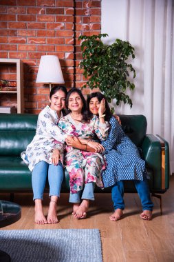 Mutlu Hintli Asyalıların portresi. Üç nesildir kanepede oturan büyükanne, kız ve kız torun.