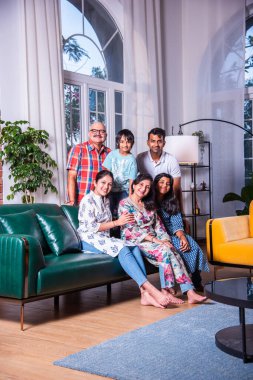 Oturma odasındaki kanepede oturan çok nesilli Hintli ailenin grup fotoğrafı.