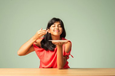 Hintli küçük kız masada otururken boş tabak sunuyor.