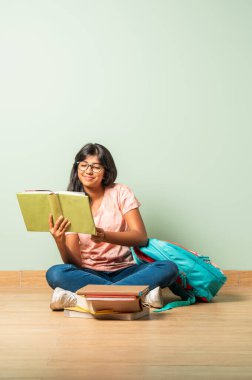 Eğitim ve okul konsepti. Küçük Hintli Asyalı kız yerde oturup kitap okuyor.
