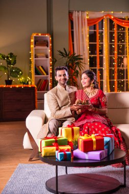 Hintli evli genç çift diwali festivalini kutluyor puja thali ve şeker tutuyorlar kanepede otururken.