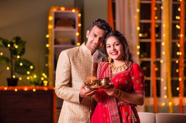 Hintli evli genç çift diwali festivalini kutluyor puja thali ve şeker tutuyorlar kanepede otururken.