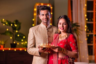 Hintli evli genç çift diwali festivalini kutluyor puja thali ve şeker tutuyorlar kanepede otururken.