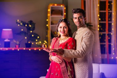 Hintli evli genç çift diwali festivalini kutluyor puja thali ve şeker tutuyorlar kanepede otururken.