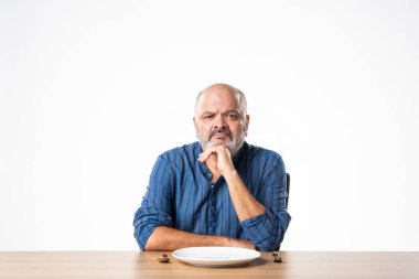 Masada otururken elinde boş seramik tabak tutan Hintli emekli yaşlı adam.