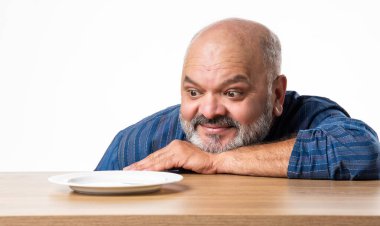 Masada otururken elinde boş seramik tabak tutan Hintli emekli yaşlı adam.